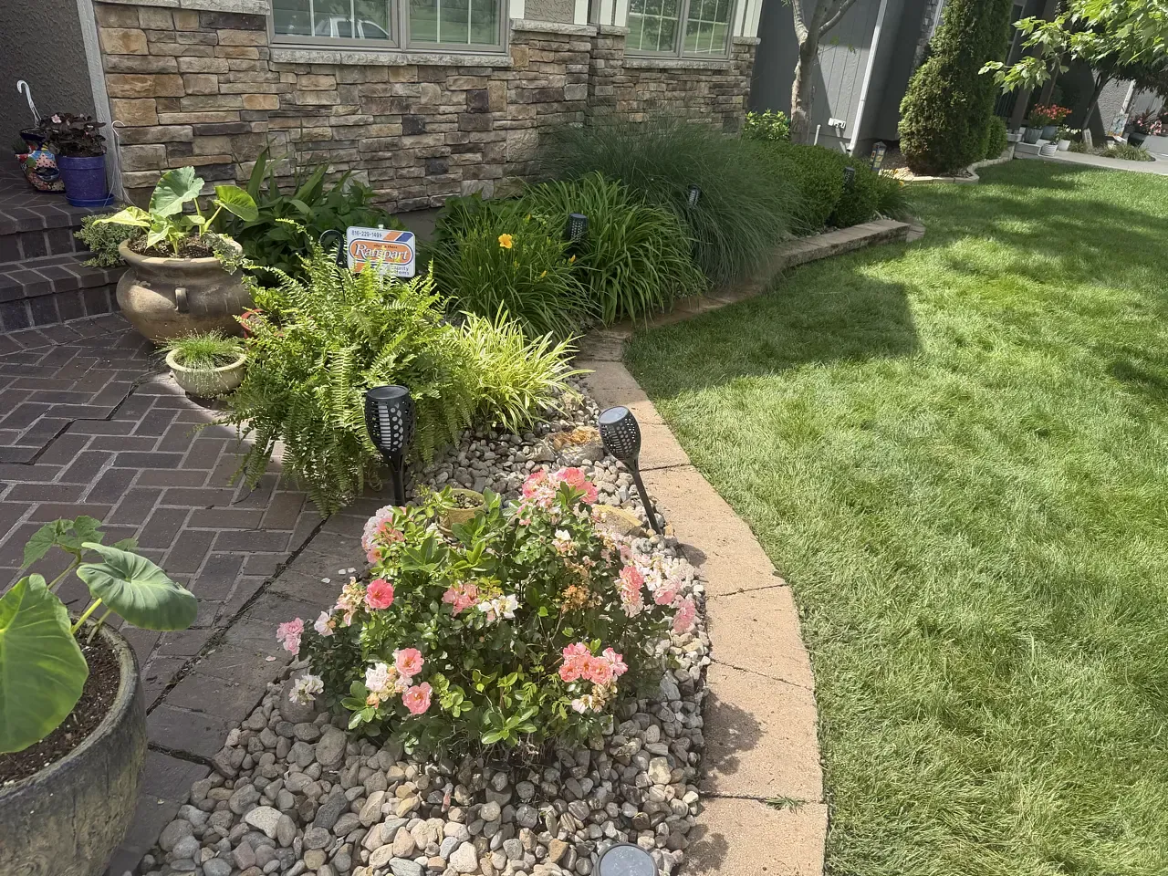A planted bed of perennials and ornamental grasses along a brick walkway, installed by Nick&rsquo;s Outdoor Services LLC